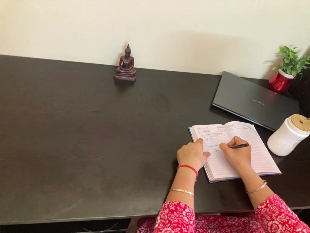 A woman writing in a simple journal beside a cup of tea on a table, bathed in soft, natural light, creating a calm and mindful atmosphere.