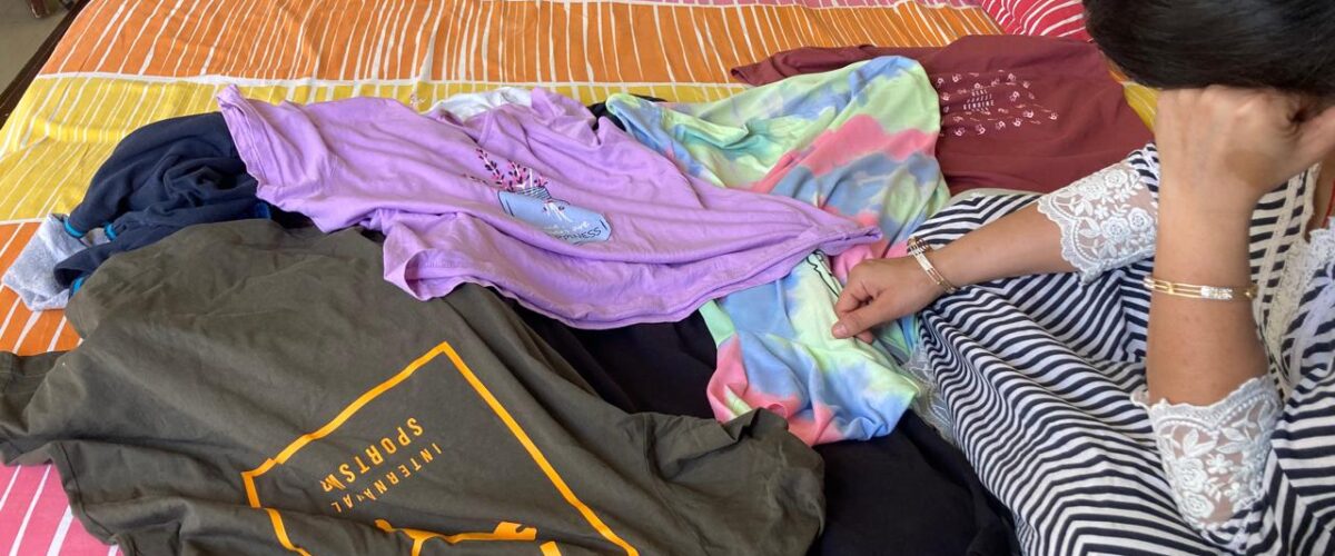 A woman holding her head in confusion while surrounded by scattered clothes, feeling overwhelmed about whether to keep or throw them away.