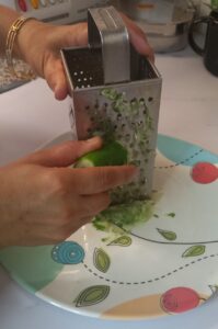 Fresh cucumber being washed and grated on a kitchen counter for Cooling Cucumber Yogurt recipe.