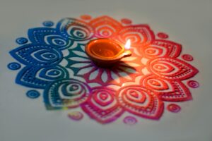 A vibrant handmade rangoli with colorful patterns and a lit diya placed at the center, creating a festive and welcoming atmosphere.