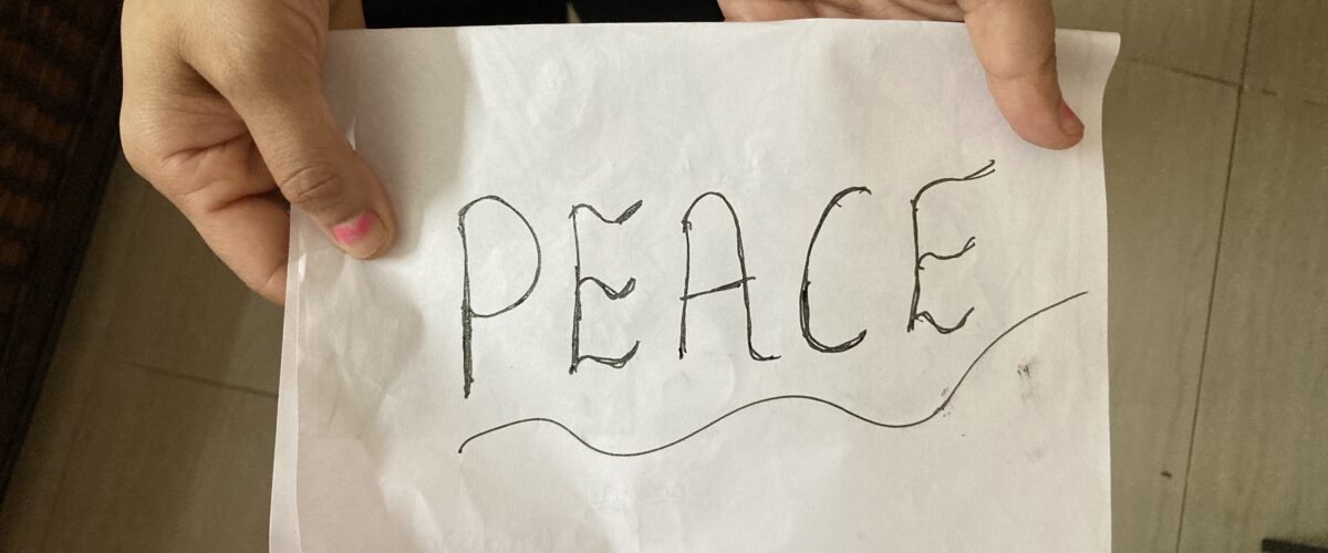 A woman holding a white paper with the word “Peace” written on it, symbolizing calm, inner strength, and simple living.