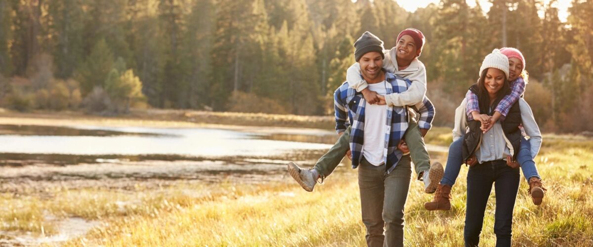 A happy mother and father carrying their kids on their shoulders while walking in a park, enjoying family time and living a simple, peaceful life.