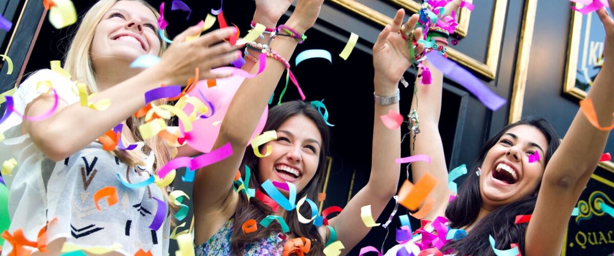 hree girls laughing together while colorful paper pieces and balloons fall around them, capturing the joy and warmth of real friendship.