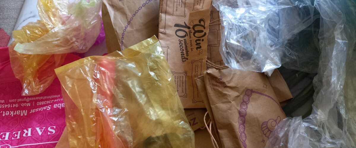 Cluttered corner filled with paper bags, plastic bags, and reusable shopping bags stacked together.