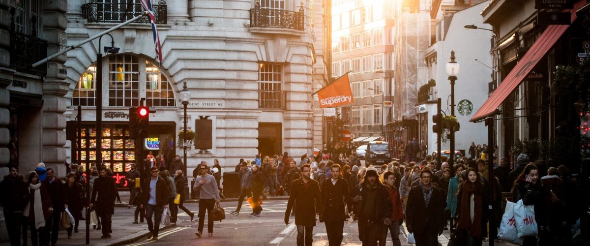 A crowd of people walking to work on a city road in the early morning, with soft sunlight rising between buildings, reflecting the quiet rhythm of daily life.