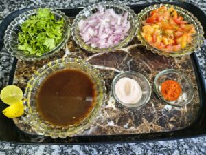 All ingredients for matar kulcha arranged on a tray — white matar, cumin seeds, chopped onion, tomatoes, ginger garlic paste, amchur and spices
