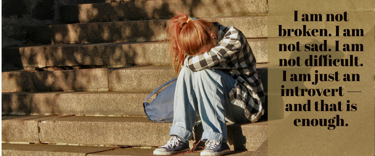A young girl sitting alone on stairs with her head resting in her lap, with the words "I am not broken. I am not sad. I am not difficult. I am just an introvert — and that is enough."