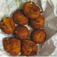 Homemade potato cheese balls served on a plate lined with paper, crispy and golden brown, photographed on a light marble surface with yellow tulips.