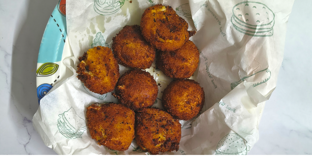 Homemade potato cheese balls served on a plate lined with paper, crispy and golden brown, photographed on a light marble surface with yellow tulips.