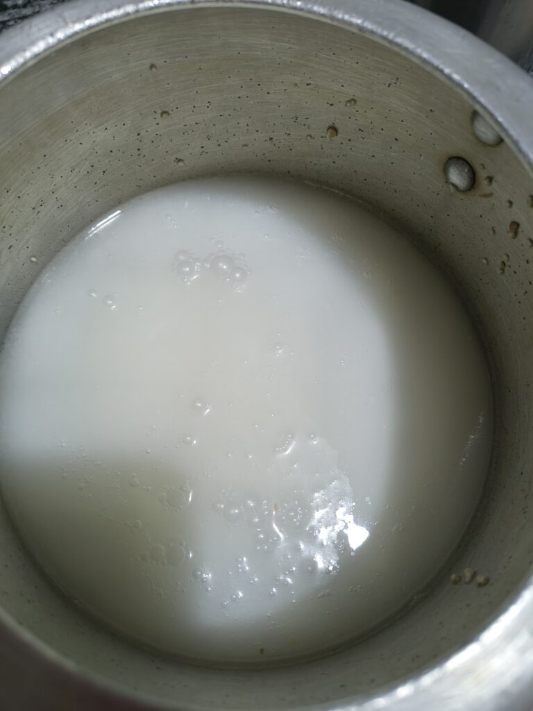 Freshly whisked, milky white chaach made from curd with small surface bubbles inside a metal pot.