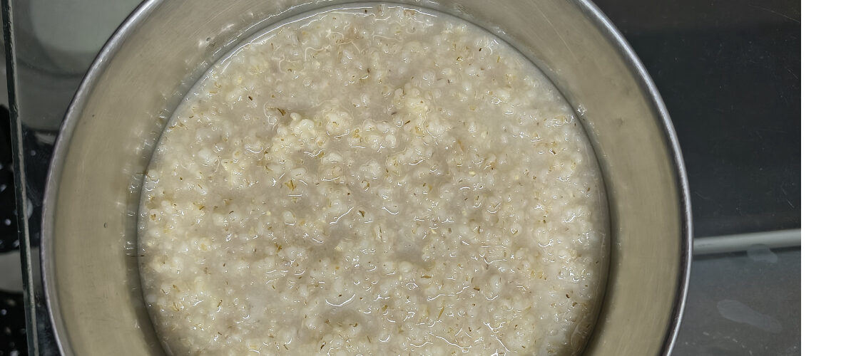 Soft, fully cooked barley groats simmering in a light liquid base inside a stainless steel pot.