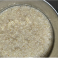 Soft, fully cooked barley groats simmering in a light liquid base inside a stainless steel pot.