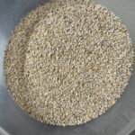A top-down view of dry, cracked barley groats filling the bottom of a clear plastic bowl.