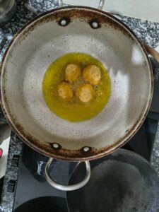 Breaded potato cheese balls frying in hot oil in a deep pan, turning golden and crispy during cooking.