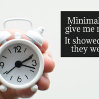 Hand holding a white alarm clock with a quote about minimalism and finding more time through intentional living.