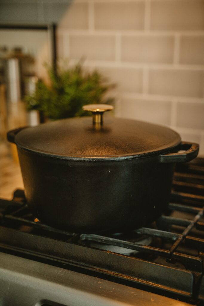 A heavy black cast iron Dutch oven with a metallic gold knob sitting on a modern kitchen gas stove burner, illustrating minimalist cookware.