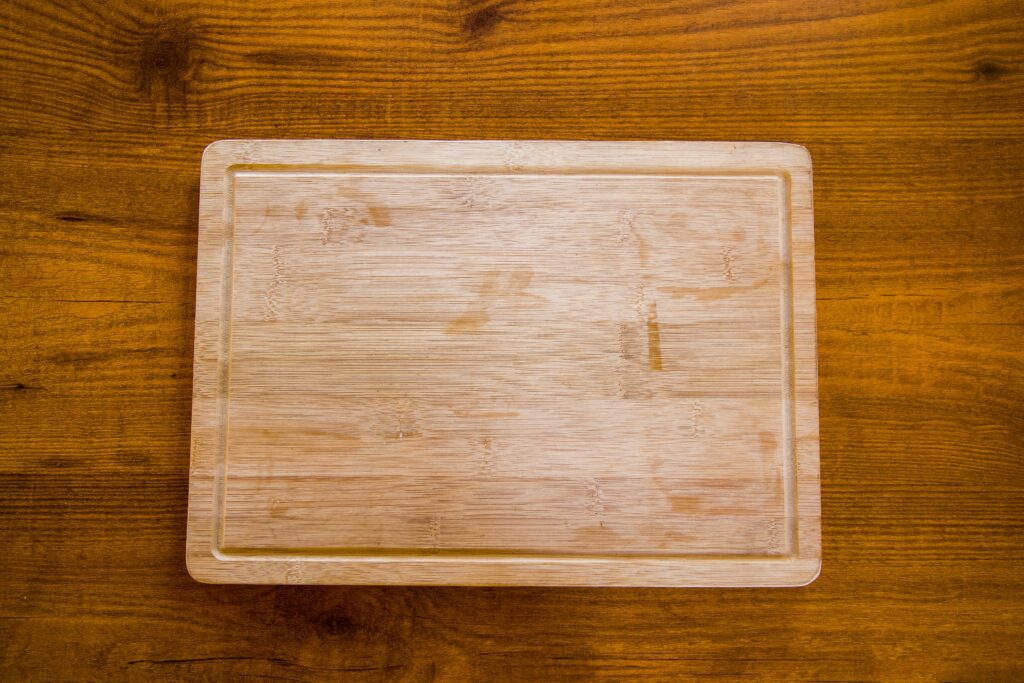 An empty rectangular wooden cutting board centered on a dark wood grain table background, showing a clean minimalist kitchen setup.