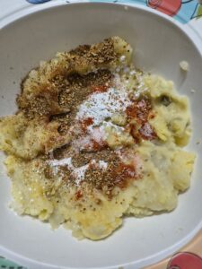Mashed potatoes mixed with salt, red chili powder, herbs, and seasonings in a white bowl, prepared as a flavorful filling for homemade potato cheese balls.