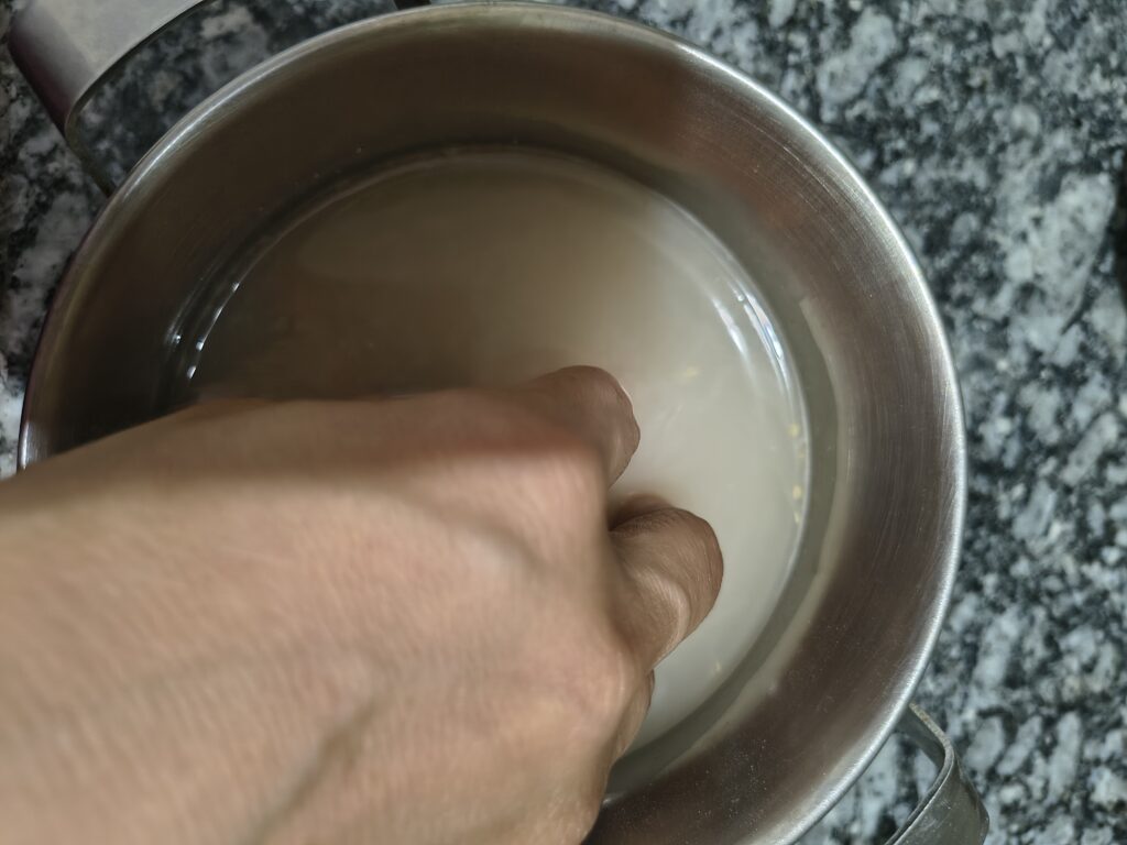 A person swishing grains of barley around in cloudy water inside a stainless steel pot to rinse it before cooking.