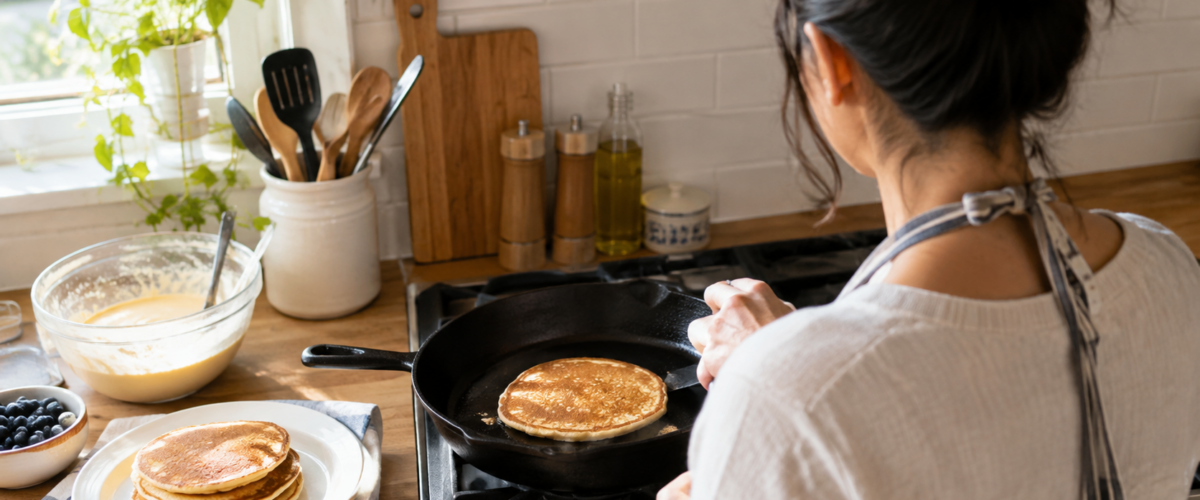 Woman cooking a pancake in a cast iron skillet in a home kitchen