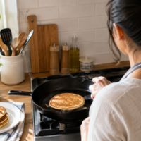 Woman cooking a pancake in a cast iron skillet in a home kitchen